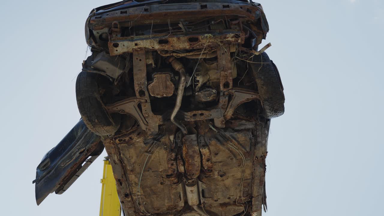 Low angle view of crane pickup up broken rusty old vehicle car in junkyard