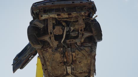 vista en ángulo bajo de la grúa que recoge el vehículo viejo y oxidado roto en el depósito de chatarra