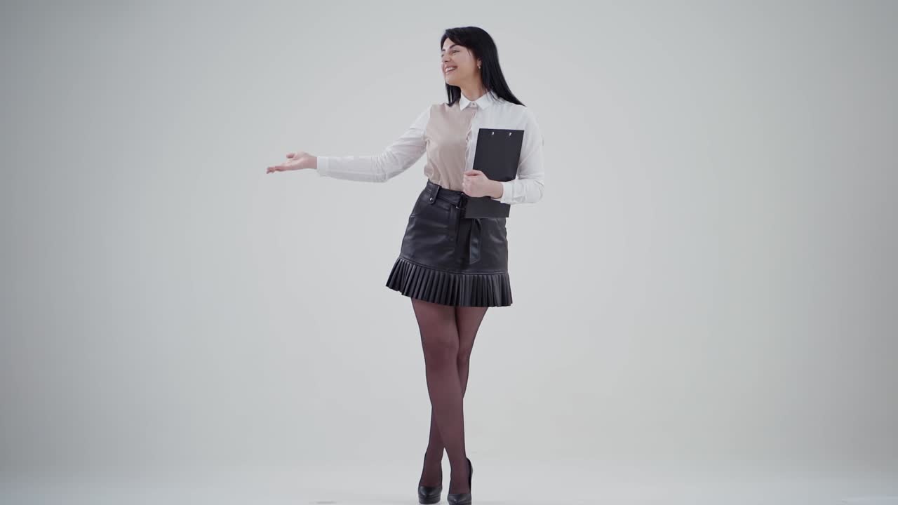 Charming young business woman in studio. Full-length portrait of smiling female in short skirt isolated on grey background holds folder. People sincere emotions.