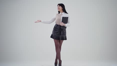 charming young business woman in studio. full-length portrait of smiling female in short skirt isolated on grey background holds folder. people sincere emotions.