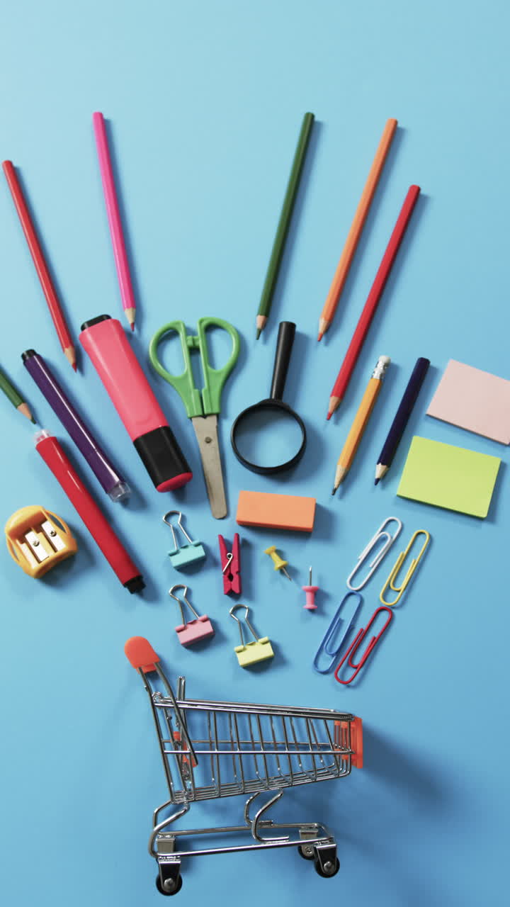 Vertical video of miniature shopping trolley with school materials and copy space on blue background