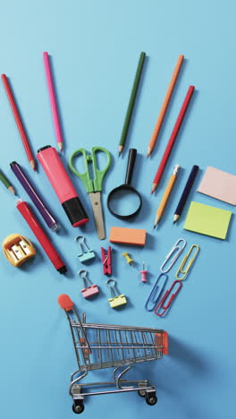 Vertical video of miniature shopping trolley with school materials and copy space on blue background