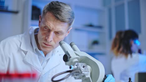 tecnólogo médico serio mirando al microscopio, escribiendo resultados de pruebas de salud