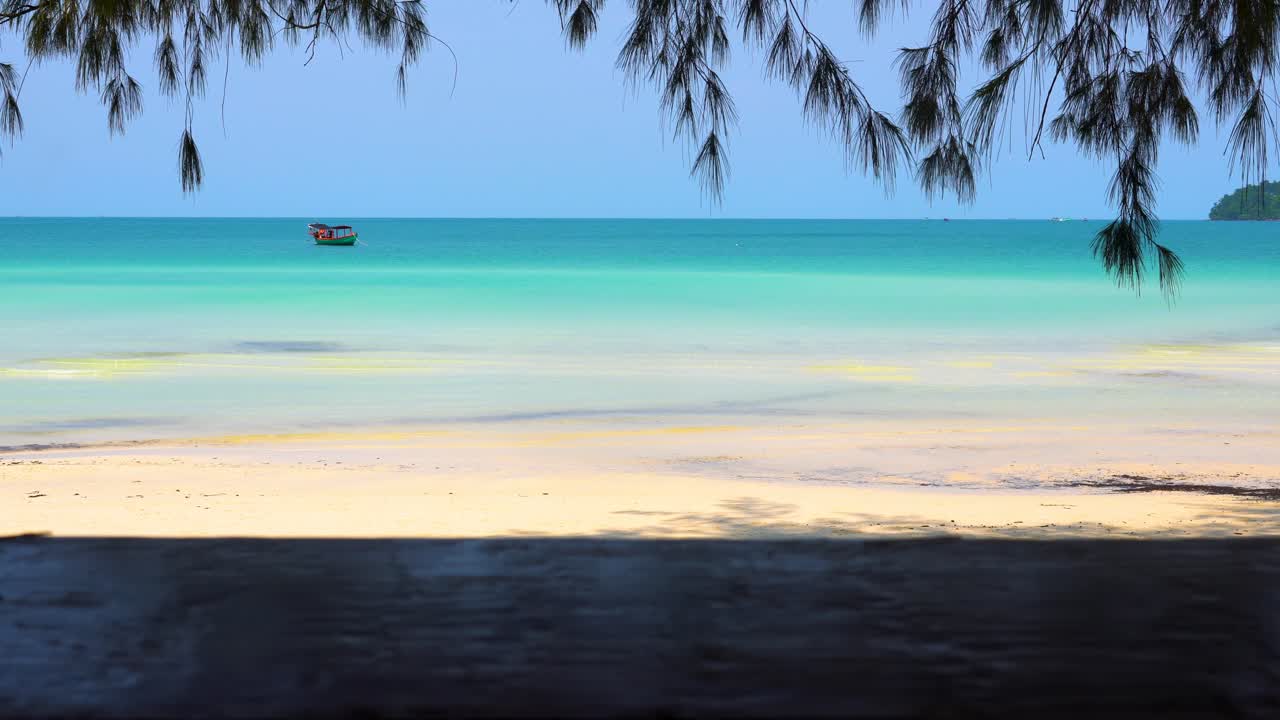 tiro de seguimiento mirando desde la orilla, imitando caminar, bajo los árboles, hacia un pequeño bote anclado en alta mar en una hermosa ubicación tropical