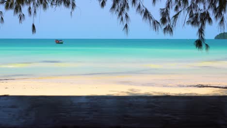 tracking shot looking out from the shore, mimicking walking, under trees, towards small boat anchored offshore in beautiful tropical location