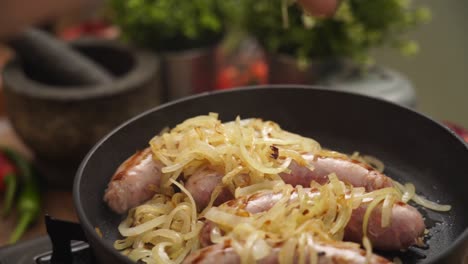 anonymous cook adding onion into pan with sausages