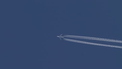 four engine jet aircraft flies across a blue sky leaving a track bright white contrails behind