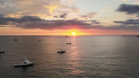botes anclados en aguas tranquilas, nubes dramáticas iluminadas por un sol dorado bajo y ardiente, panorámica aérea hacia arriba