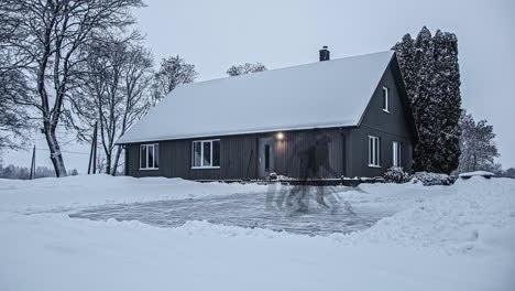 Low-angle-shot-of-a-man-clearing-with-a-shovel-clearing-snow-in-front-of-a-suburban-wooden-cottage-after-a-heavy-snowfall-on-a-winter-day