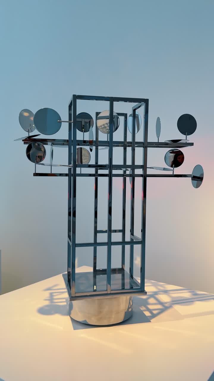 Modern abstract metal sculpture with circular mirrors in museum. A geometric chrome sculpture with rotating circular mirrors on a white pedestal in a gallery setting
