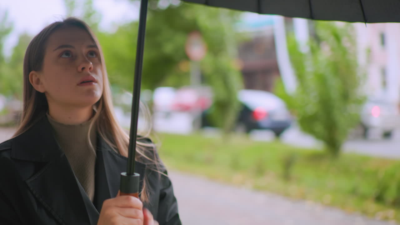 Primo piano di persona con cappotto nero che tiene un ombrello nero mentre si prepara ad aprirlo all'aperto in una giornata piovosa, a simboleggiare protezione, anticipazione, preparazione al meteo, resilienza, riparo, sicurezza personale