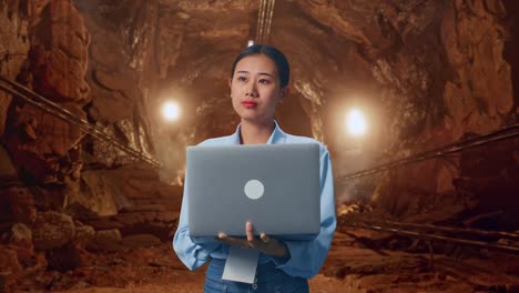 asian female with her laptop in underground mine tunnel, she observes by looking around before she come to concentrating with her laptop