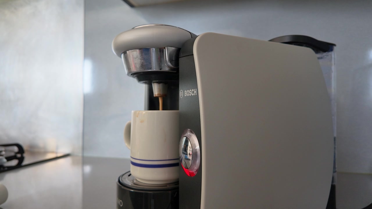 Tomada em close-up de uma cafeteira moderna preparando café expresso fresco em uma caneca branca.