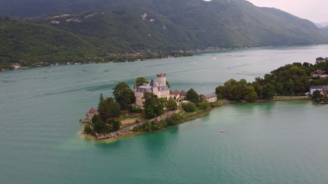 Aerial drone footage rotating slowly around Château de Duingt castle with the stunning views of lake Annecy and the surrounding mountains behind
