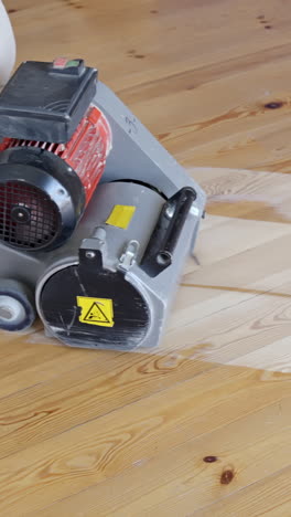 vertical footage shows sanding machine actively working on a pine floor, with dust and sanding marks visible, focus on machinery details and floor texture, captured in real time during renovation.