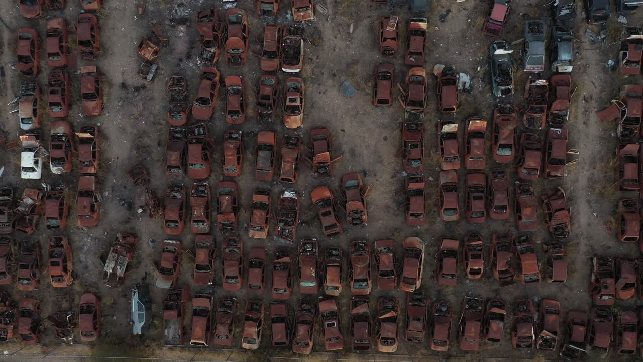 Tembakan close-up udara zenital dari kiri ke kanan dari tumpukan mobil rongsokan yang ditinggalkan