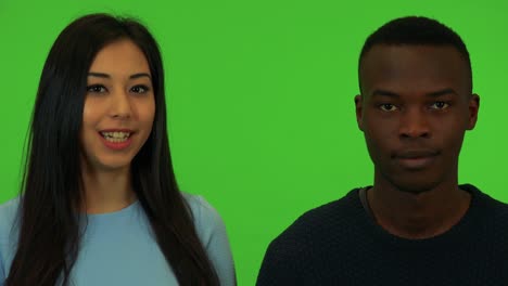 a young asian woman and a young black man talk to the camera - closeup on the faces - green screen studio