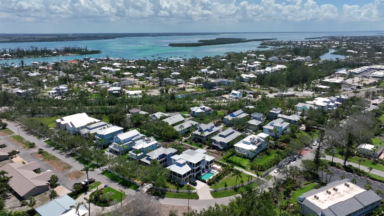 Aerial view of Coquina Beach, featuring a picturesque coastal community with a mix of residential areas surrounded by lush greenery and waterways. The scene captures bright blue skies and serene water