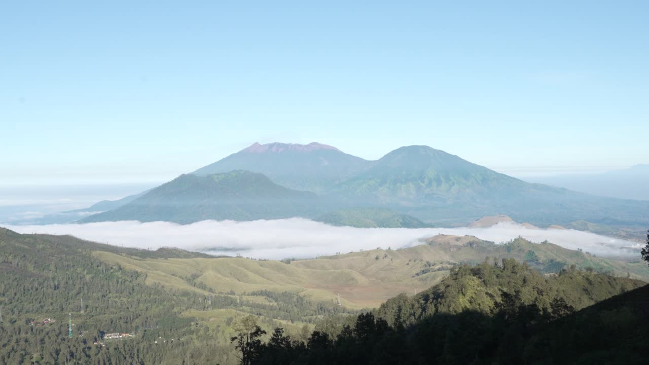 Pemandangan luas Gunung Berapi Raung dengan kabut pagi di atas lembah hijau di Indonesia