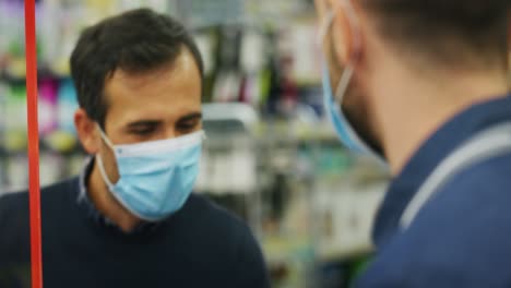 authentic shot of male customer and male cashier wearing medical masks to protect themselves from disease while paying with credit card grocery food products in supermarket.