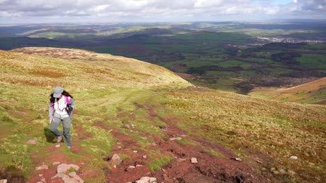 mujer caminando en un día de viento en el parque nacional de brecon beacons con una cámara, gales