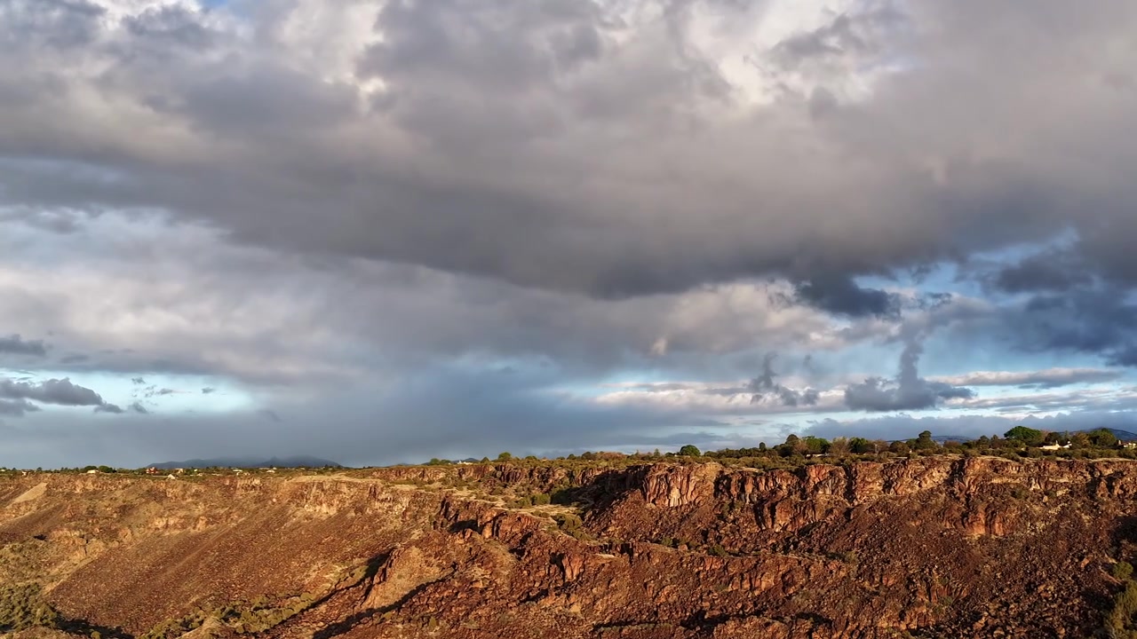 Timelapse de drone 4K captura um voo ao nascer do sol ao longo de uma crista de cânion acidentada sob céus tempestuosos. O movimento cinematográfico revela nuvens escuras em deslocamento e um horizonte laranja vibrante sobre um precipício desértico.