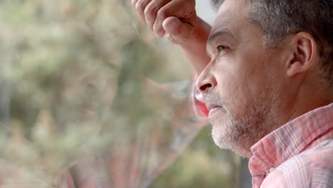 thoughtful senior biracial man looking out of window at countryside, copy space, slow motion