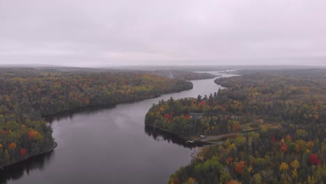 drone shot flying over a gorgeous river surrounded by trees changing color in the fall time