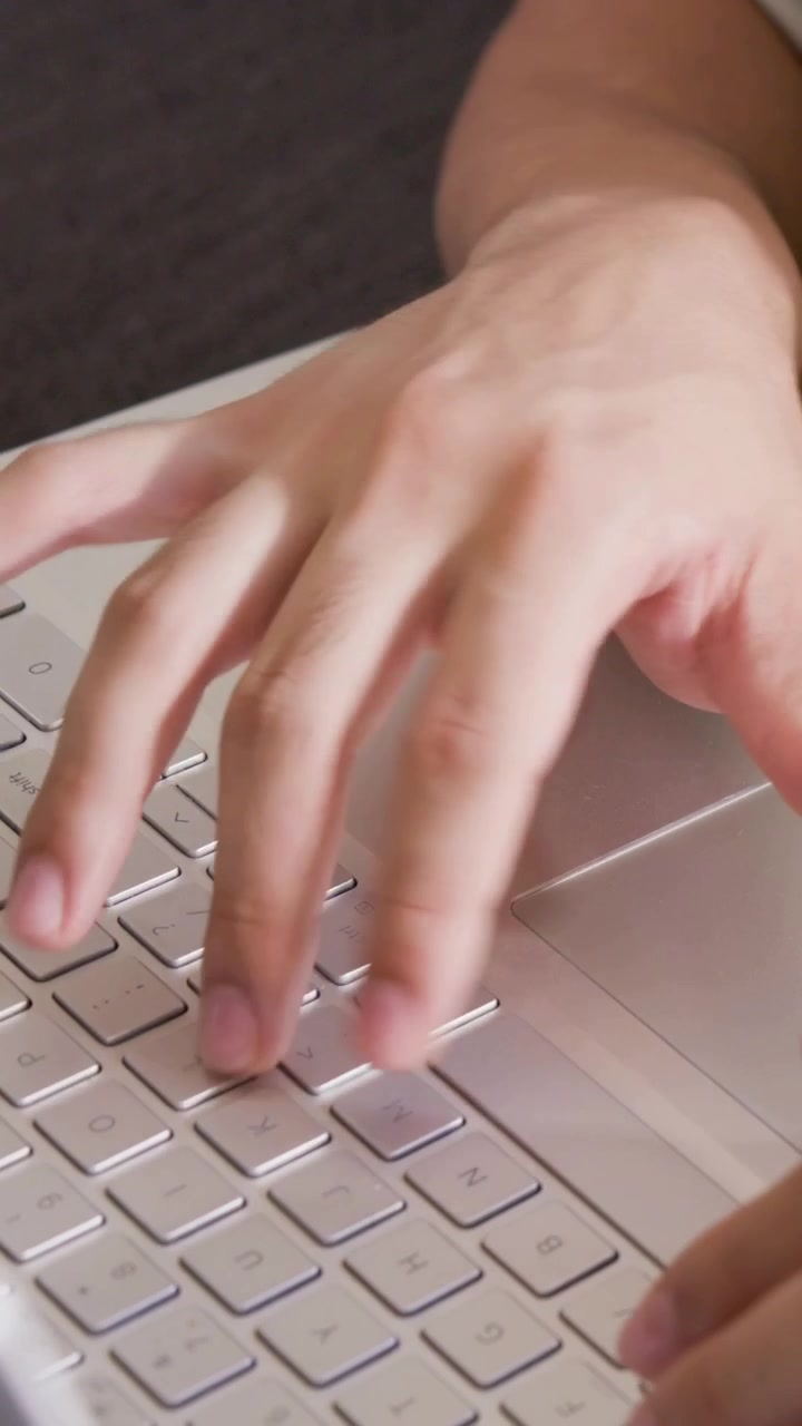 Vertical video: Landing man's hands and arms starting typing and using trackpad on couch in Tshirt