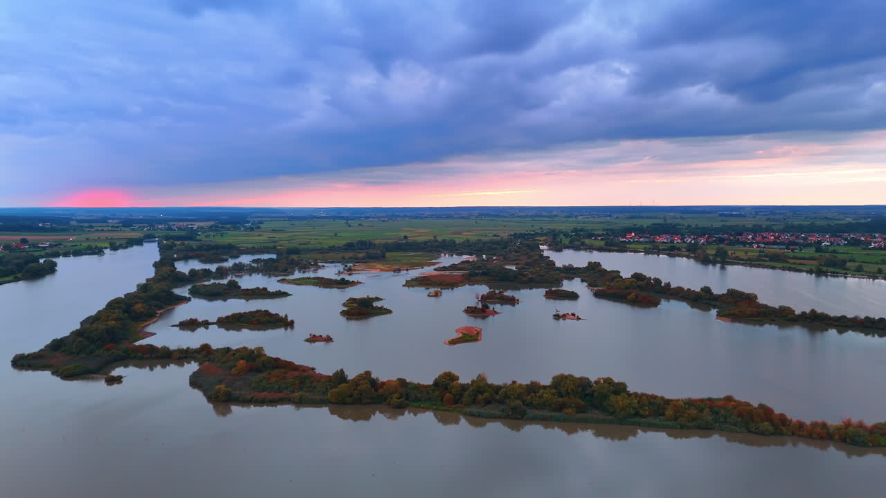 Drone view of small islands in calm lake at sunset. Aerial panorama of small islands in a peaceful lake surrounded by countryside during evening light