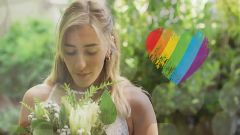 animation of rainbow heart over caucasian woman wearing wedding dress and holding flowers
