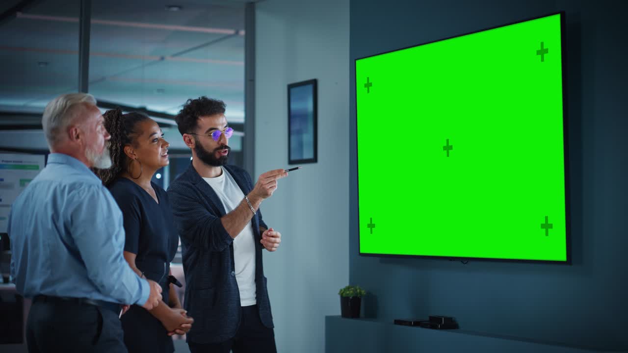 Company Operations Manager Holds Meeting Presentation for a Team of Executives. Adult Male Uses Wide TV Set with Horizontal Green Screen Mock Up Display. People Work in Business Office.