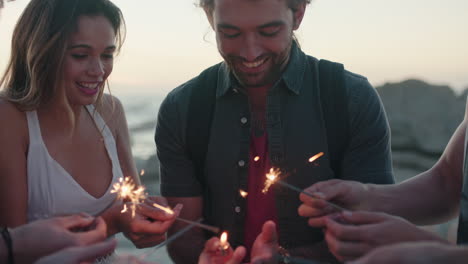 happy group of friends celebrating new year with sparklers on beach at sunset