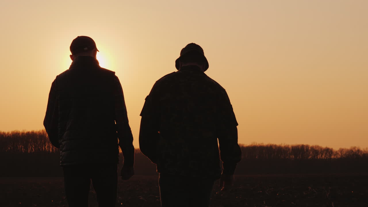 Due agricoltori camminano attraverso il campo al tramonto, chiacchierando. Startup nell'agribusiness.