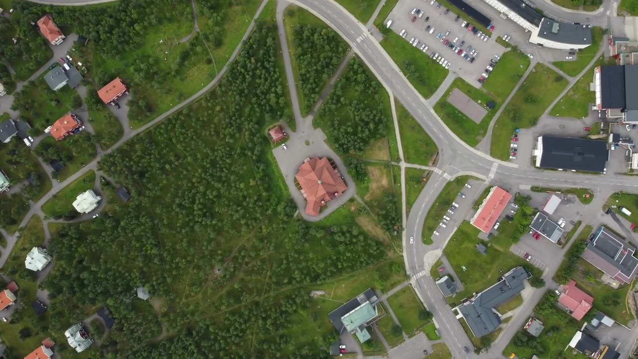 Filmato aereo dall'alto scende e ruota sopra la Chiesa di Kiruna con il tetto rosso in Svezia, circondata da foreste, strade tortuose, aree di parcheggio ed edifici vicini.