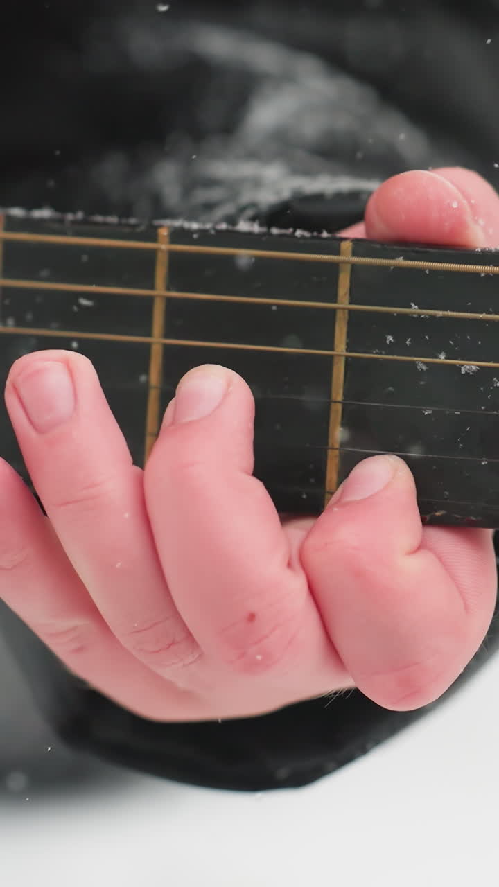 primer plano de la mano tocando la guitarra en cuerdas de polvo de nieve, mezclando la música y la belleza del invierno, mostrando la armonía artística con detalles helados en el cuello de la guitarra y el fondo blanco sereno