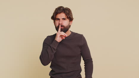frightened young man closing mouth with hands refusing to tell terrible secret on beige background