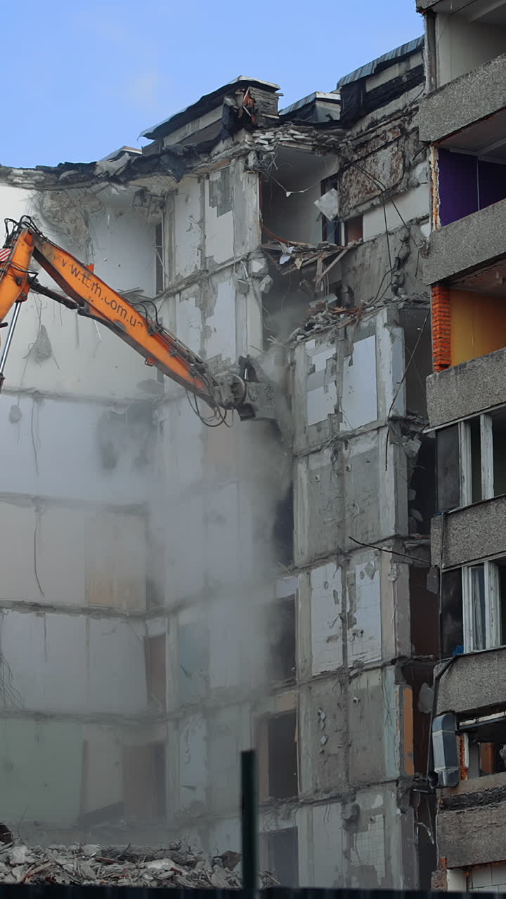Compact orange demolishing machine dismantling the house. Deconstruction of a building ruined by the nature disaster. View from below. Vertical video
