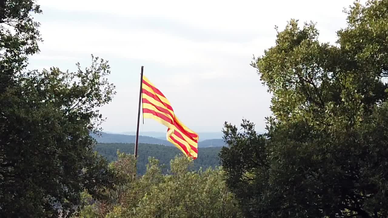 cámara lenta de la bandera catalana en la cima de una colina, con vistas a las colinas con un cielo nublado