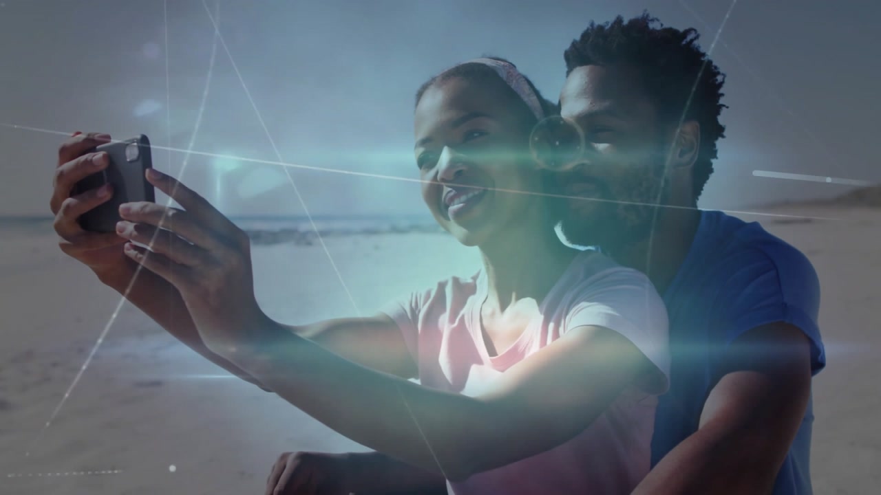 Couple taking selfie at shoreline, using smartphone technology with light streaks and lens flare