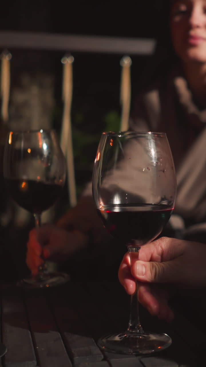 Man and woman clink wineglasses on night rooftop closeup. Romantic couple cheers glasses of red beverage at low table on restaurant terrace in evening