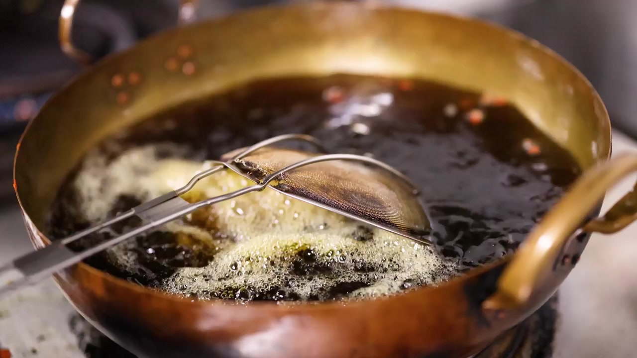 Close-up of a chef deep frying snacks in hot oil using a brass wok.