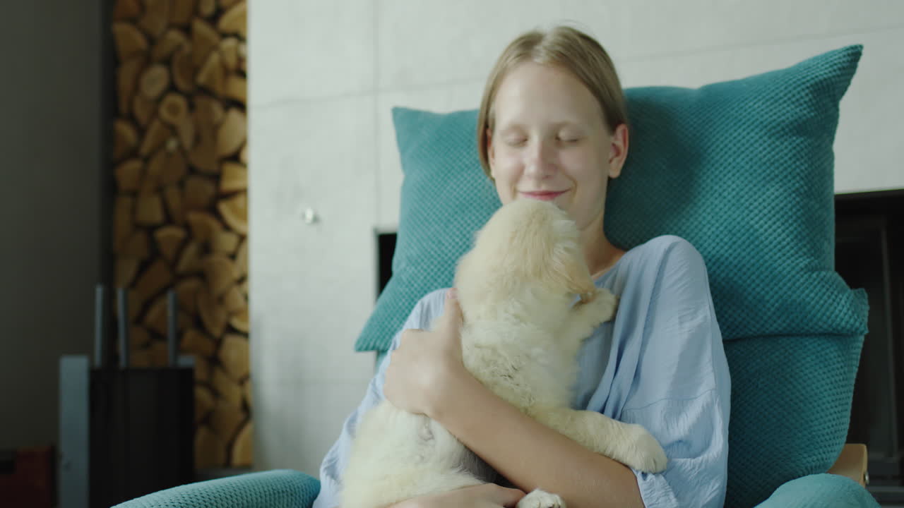 십대 소녀는 골든 리트리버의 강아지와 함께 놀고, 벽난로 근처의 의자에 앉아 있습니다.