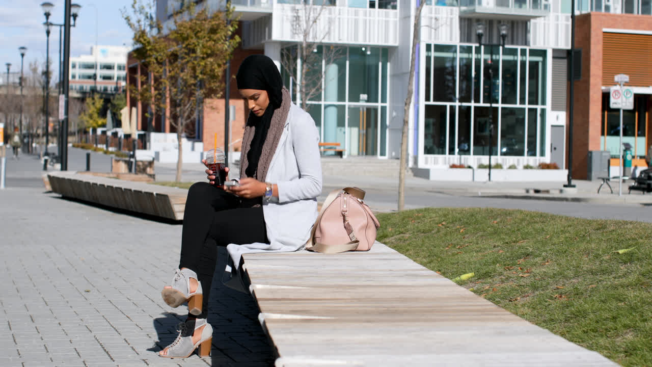 Side view of young Asian woman in hijab using mobile phone in the city 4k
