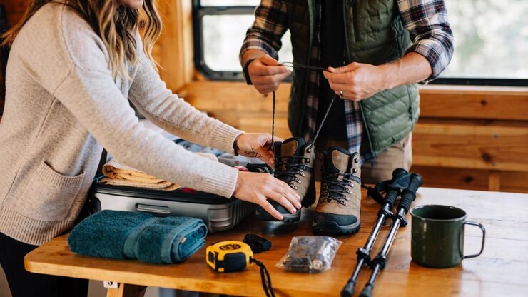 Packing couple in cardigan, vest prepping gear for hike on cabin table, tying boots