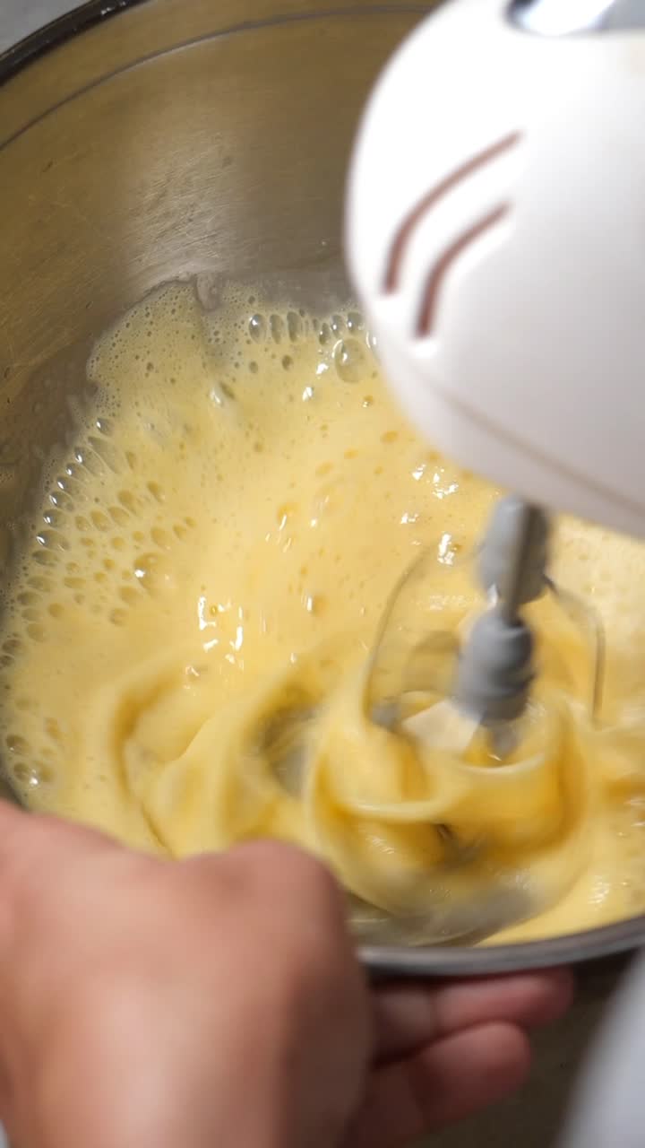 Close-Up of Hand Mixing Eggs with Electric Mixer in Bowl
