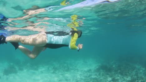 a girl in a swimming costume snorkelling in tropical waters while using an underwater camera