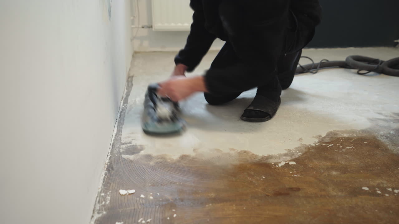 A person is working on a home renovation project by grinding and smoothing the floor. The task involves using a machine to prepare the surface in a room. Dust is produced during the work