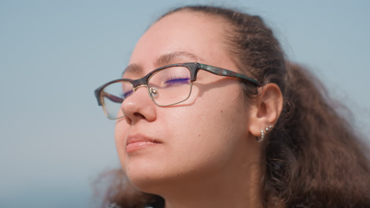 Donna con occhiali sulla spiaggia, con un'espressione contemplativa che varia nelle diverse scene: una studentessa che disegna, una scrittrice che sogna ad occhi aperti, una viaggiatrice che ammira l'oceano, una pensatrice che riflette sullo skyline, il tutto sotto una calda luce solare.