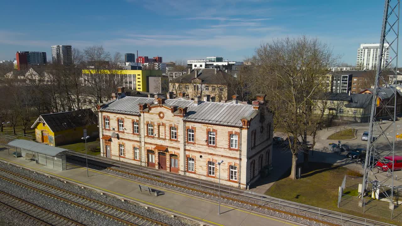 Drone aerial around outdoors railway station with low platform and train tracks. Old style railroad station, symmetrical building with brick facades, rustic stone station building at Tallinn Vaike